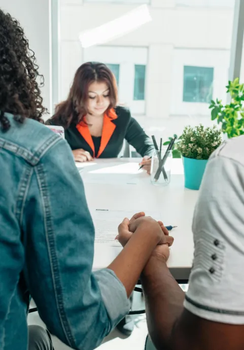 Couple holding hands during an adoption meeting with a social worker in an office setting.