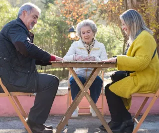 Three seniors enjoying a sunny day playing dominoes outdoors in a Portuguese park.