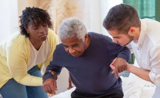 An elderly man receiving assistance from caregivers in a cozy home environment.
