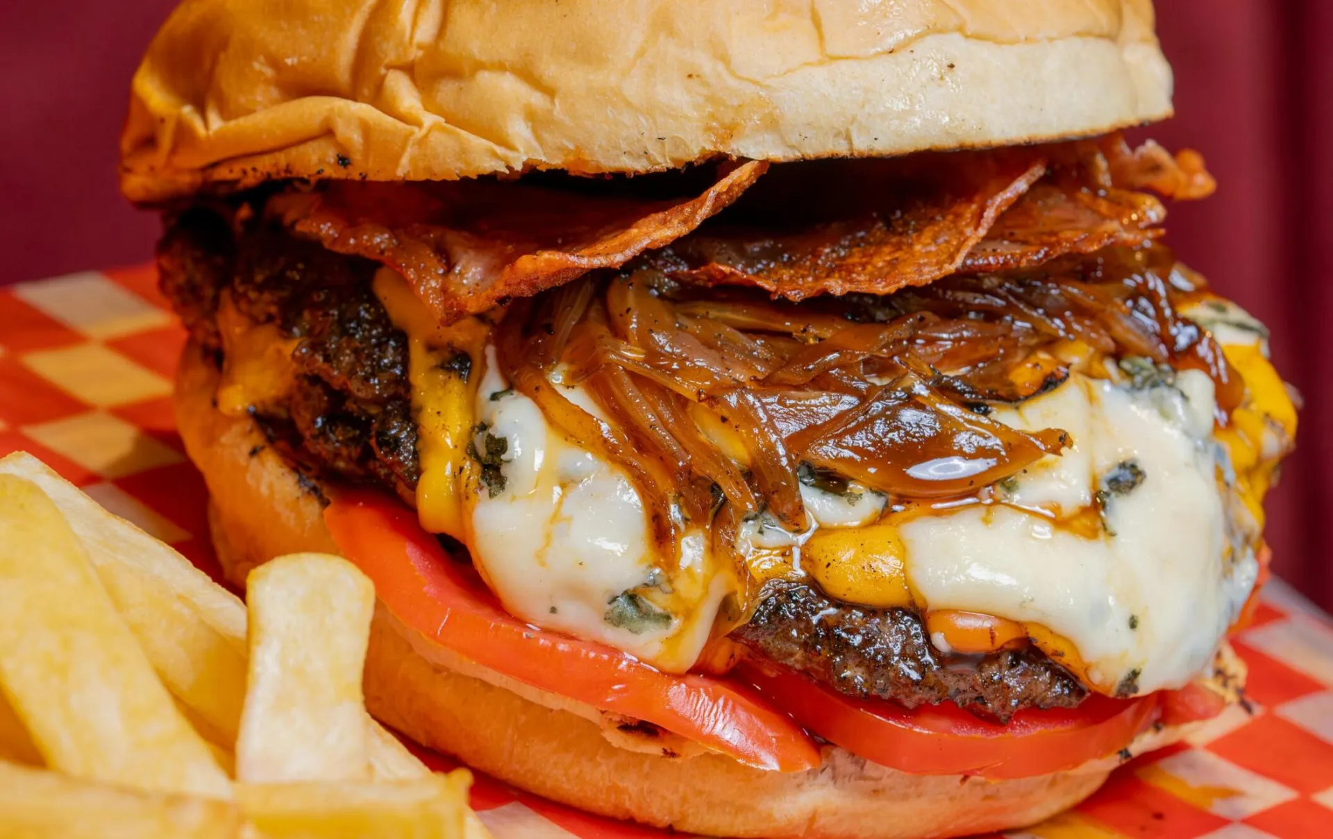Close-up of a juicy beef burger with melted cheese and crispy bacon served with french fries.