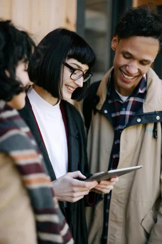 Group of young adults smiling and using a tablet outdoors.