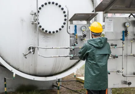 A worker in safety gear operates a large industrial machine outdoors, ensuring operational safety.