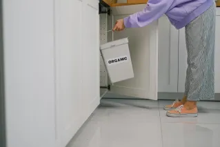 A person placing an organic waste bin inside a modern kitchen cabinet, promoting sustainable living.