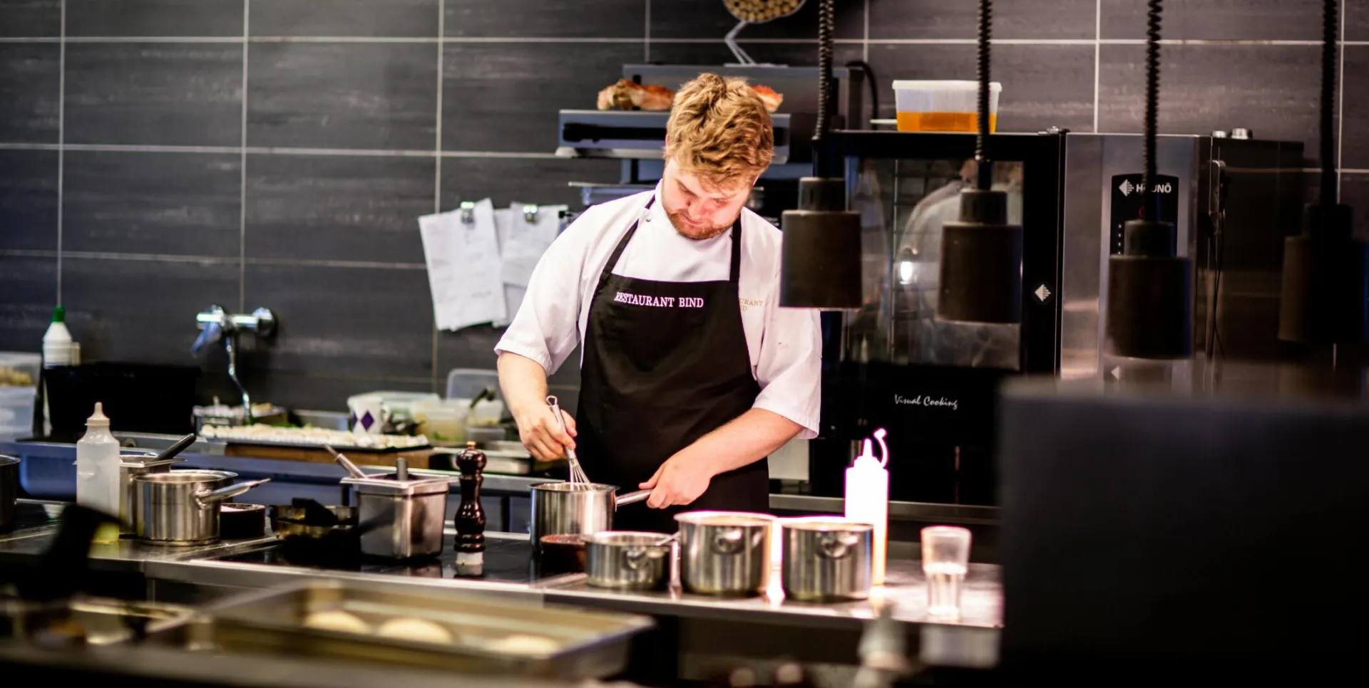 Chef preparing meal in a modern kitchen with various cookware.