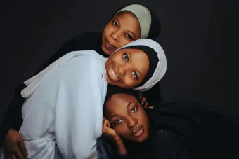 Three women in hijabs smiling and embracing, showcasing unity and tradition.