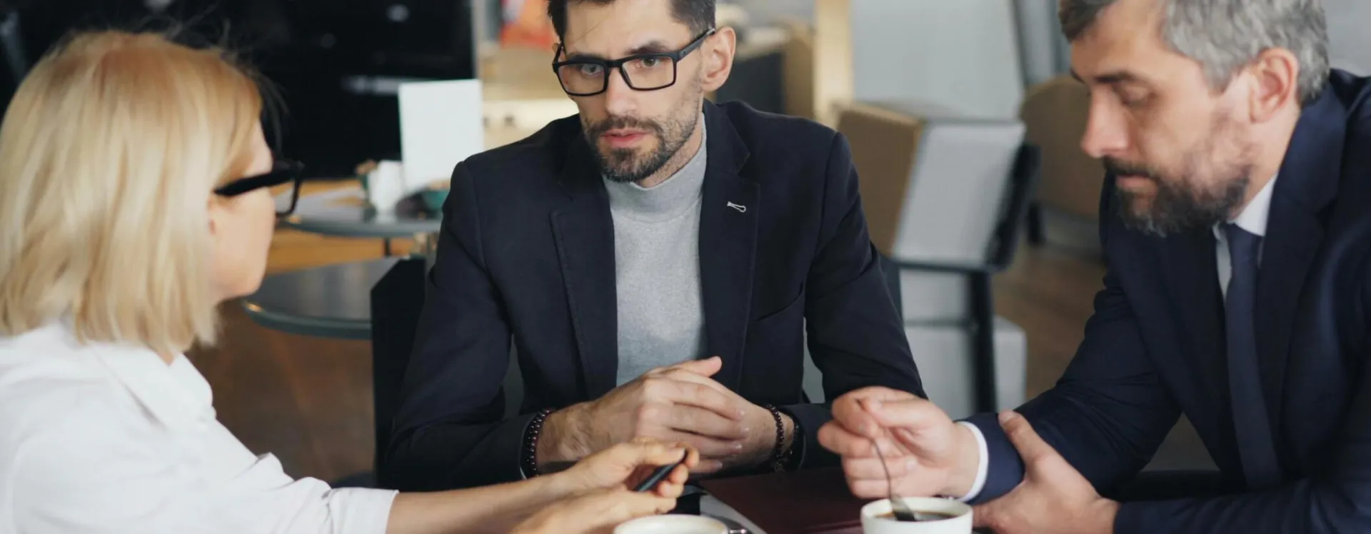 Professional meeting with three businesspeople discussing strategy over coffee in a modern café.