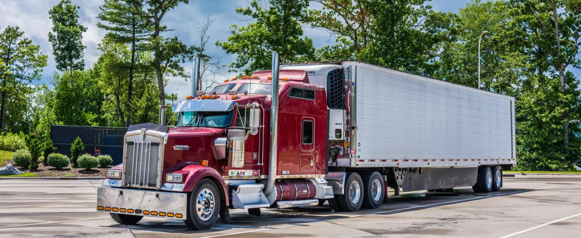 A striking red semi truck parked in a lush scenic area, showcasing modern transportation technology.