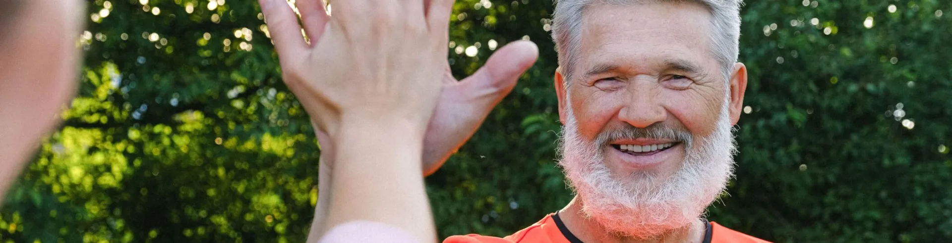 Cheerful aged man in bright clothes smiling and giving high five  to friend in sunny day