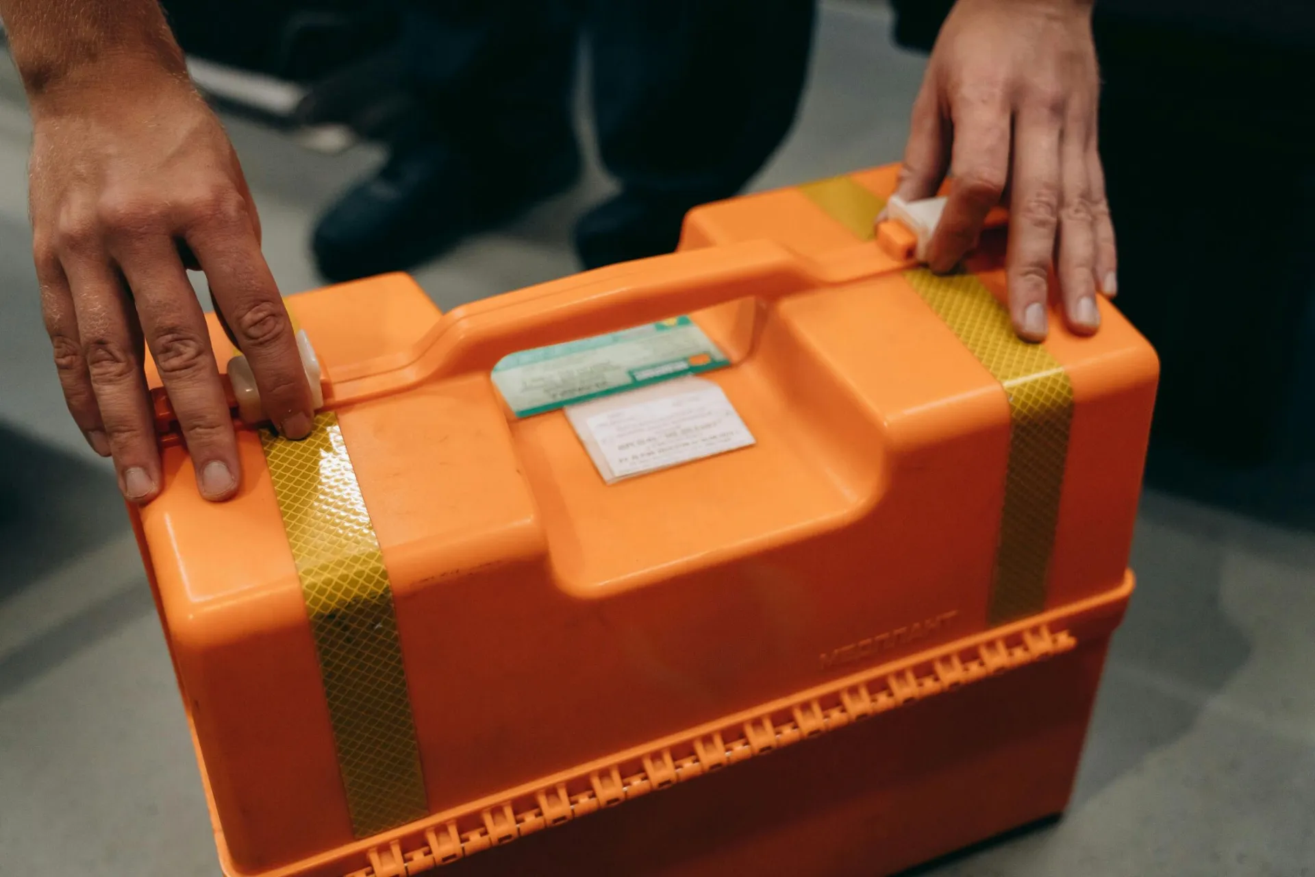 Close-up of hands holding an orange emergency medical kit indoors.