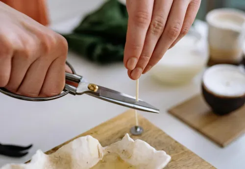Close-up of a person cutting a cotton wick for a handmade candle in a shell mold. DIY creativity.