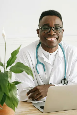Friendly African American doctor smiling with stethoscope and laptop in an office setting.