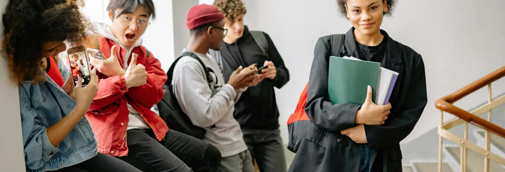 A group of diverse college students using smartphones and chatting in a hallway, representing modern student life.