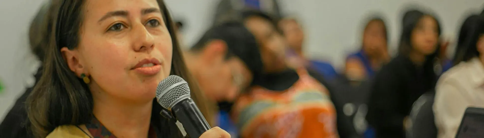 Young woman with microphone speaking during a classroom presentation with students.