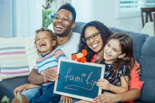 Cheerful family with kids holding a chalkboard at home, showcasing togetherness and love.