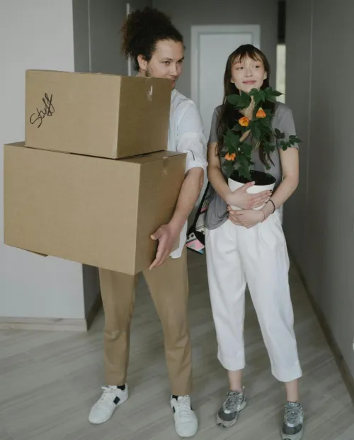 A young couple carrying boxes and a plant into their new home, symbolizing a fresh start.