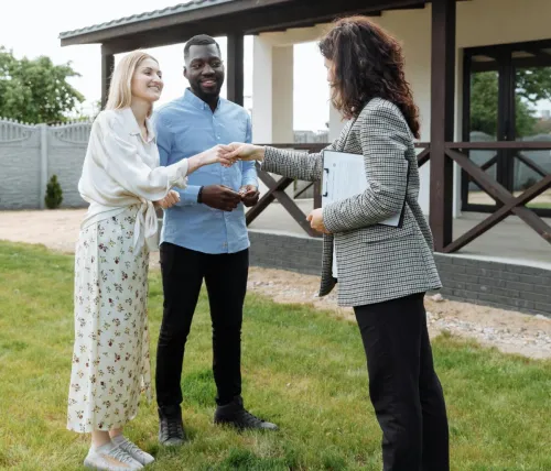 A realtor finalizes a home sale with a handshake agreement, welcoming new homeowners to their property.