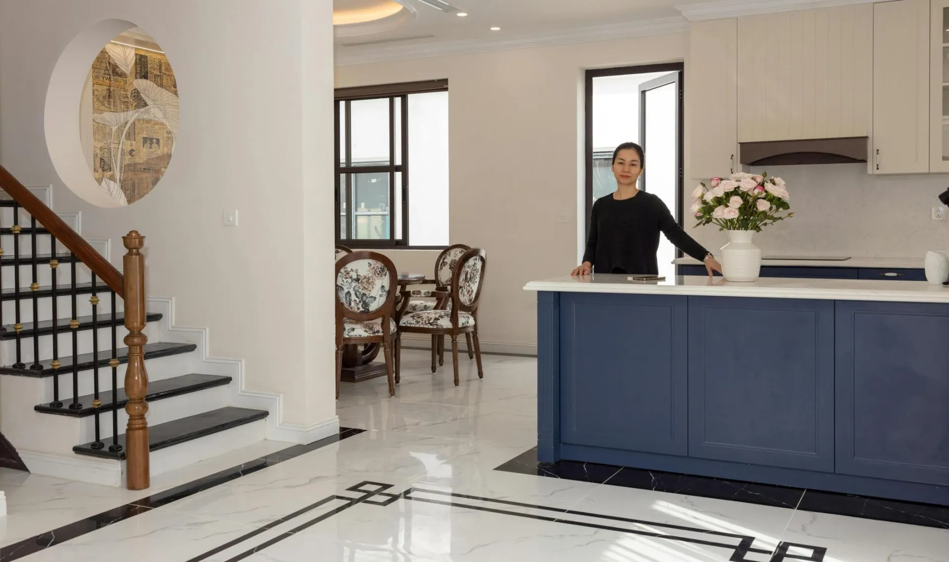 Spacious modern kitchen with a woman standing, elegant floral decor and stylish furniture.