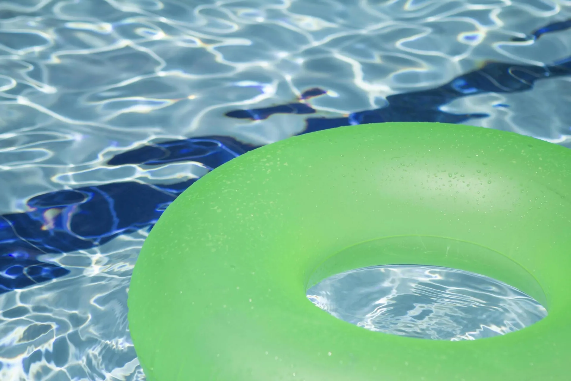 A vibrant green inflatable swim ring floating in a refreshing blue swimming pool.