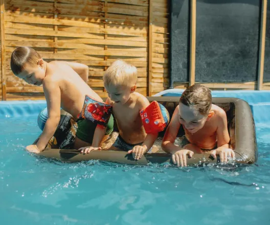 Three children playing in a pool with inflatables on a sunny summer day.