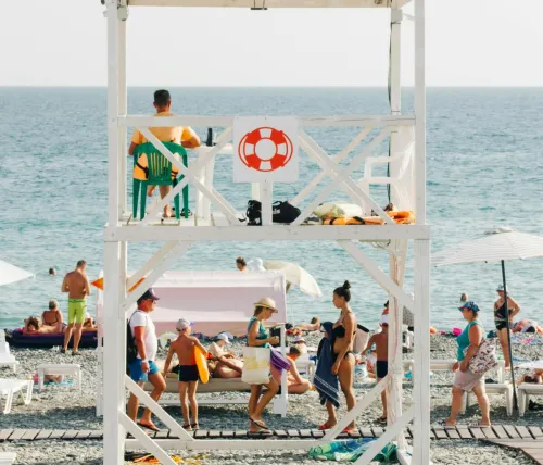 A lively beach with a lifeguard tower overseeing families enjoying a sunny day by the sea.