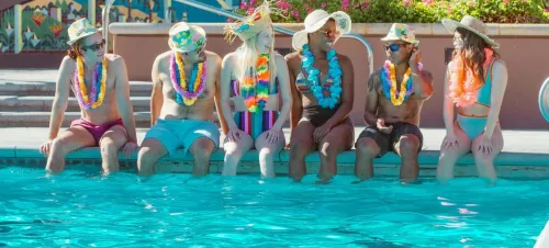 A group of diverse friends enjoying a lively summer pool party, sitting poolside with leis and sun hats.