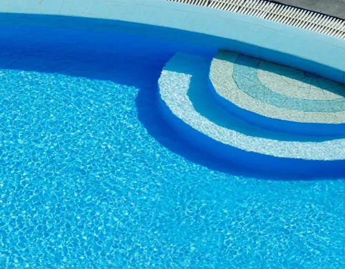 Sun-drenched swimming pool captured from above, showcasing clear blue water and elegant curves.