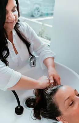 A professional hairstylist washing a woman's hair in a modern salon setting, ensuring quality haircare.