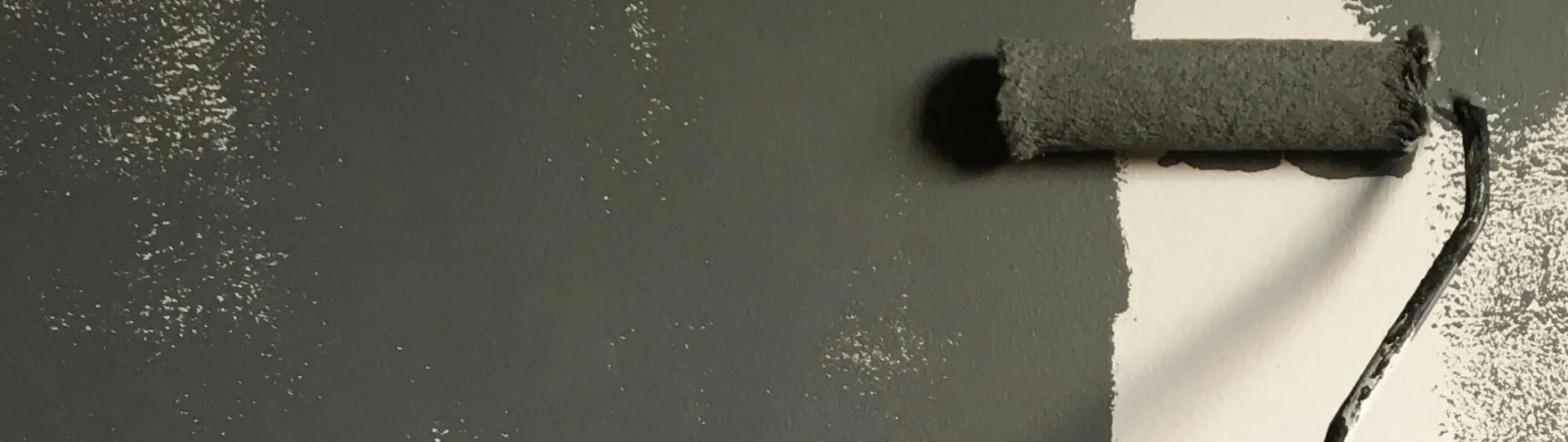 A hand painting a wall gray with a roller during a house renovation project.