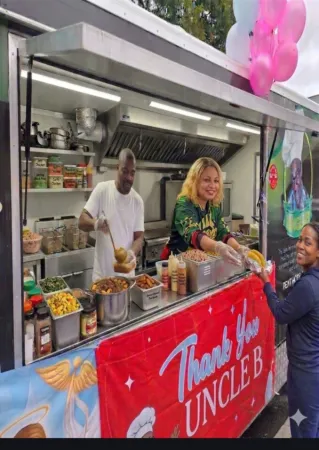 A man and woman stand in front of a food truck, offering street food at night.
