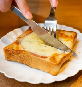 Close-up of a grilled cheese toastie being cut open, served on a white plate in Tokyo.
