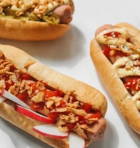 Three gourmet hot dogs with various toppings captured in a clean, appetizing close-up.