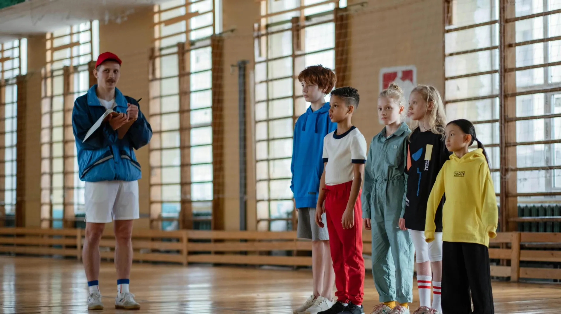 A coach instructing a diverse group of children during a gym class in a school sports hall.