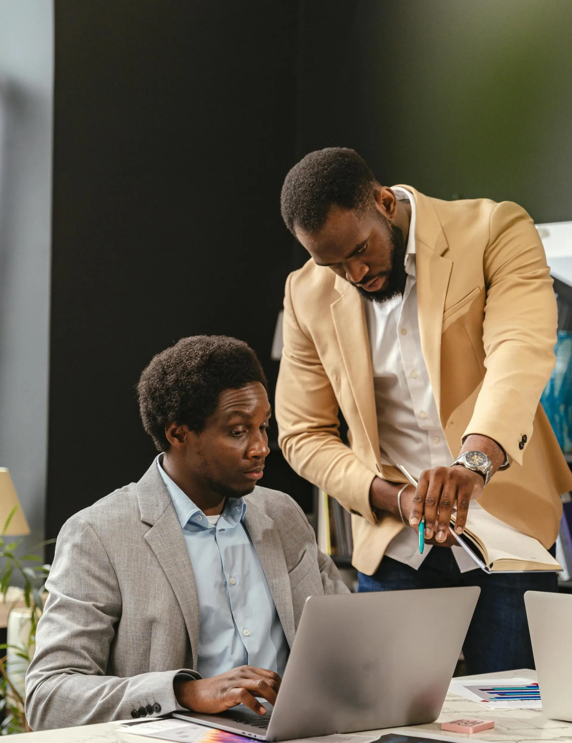 Two business professionals working together in an office space with laptops and papers.