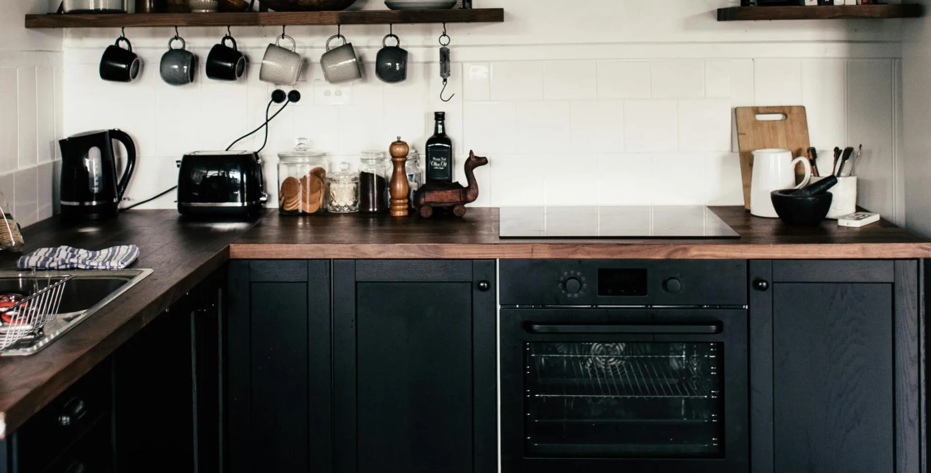 Interior of contemporary kitchen with black wooden cupboards and shelves with various utensils and appliances