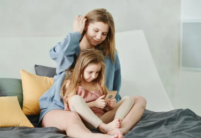A mother and daughter spending quality time together, sitting on a cozy bed indoors.