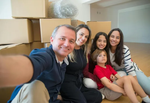 A family smiling and taking a selfie among moving boxes in their new home.