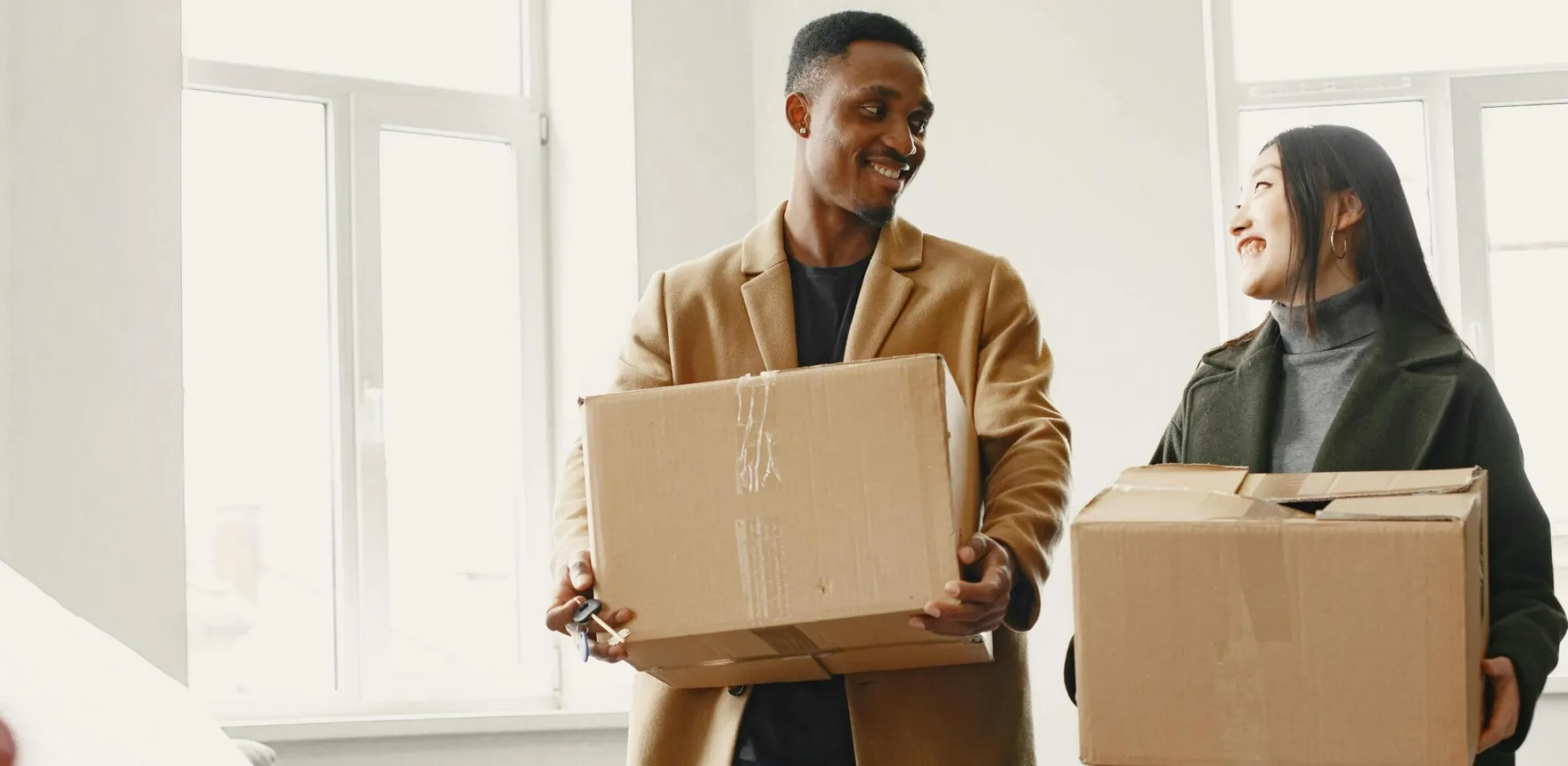 Happy couple carrying moving boxes into their new home, symbolizing a fresh start.