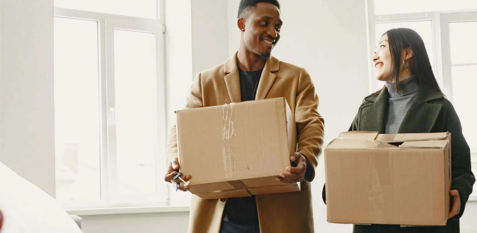 Happy couple carrying moving boxes into their new home, symbolizing a fresh start.