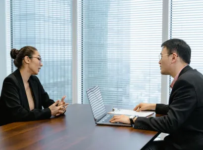 Two colleagues in a professional meeting discussing business strategy at an office table.