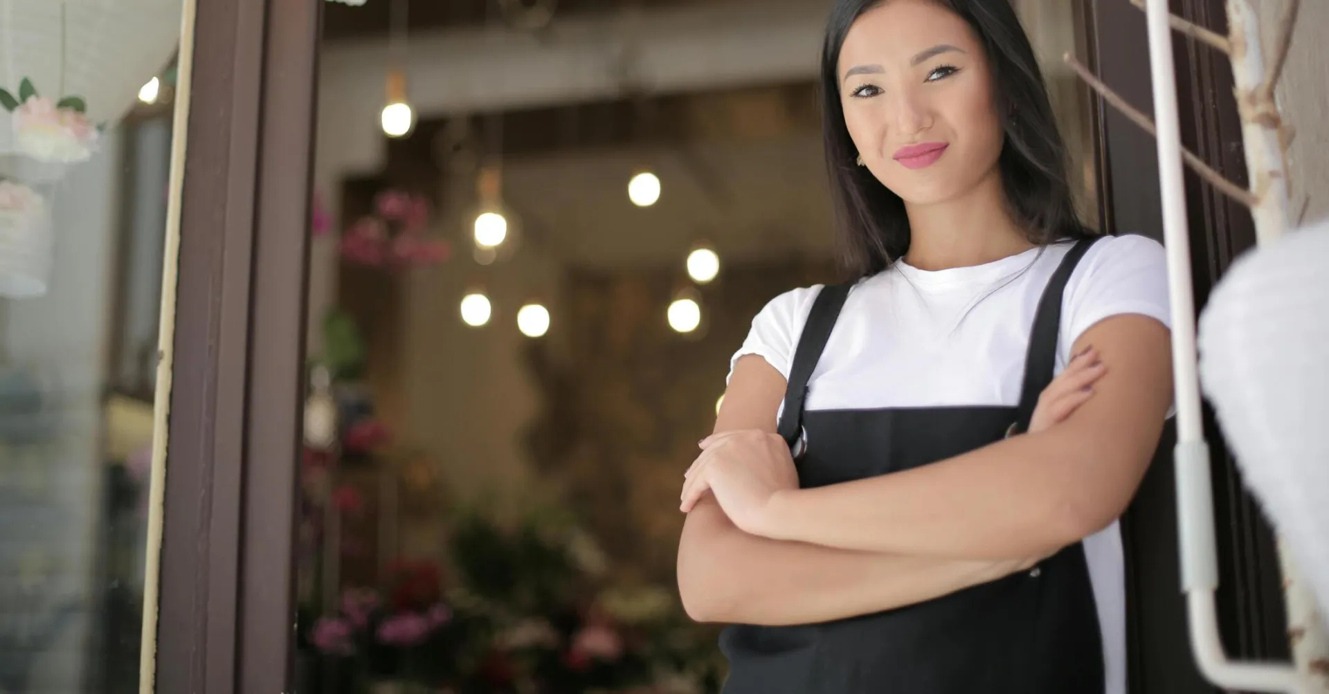 Smiling female florist standing with arms crossed at shop entrance, exuding confidence and friendliness.