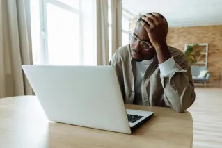 Man stressed while working on a laptop indoors, dealing with issues in remote work.