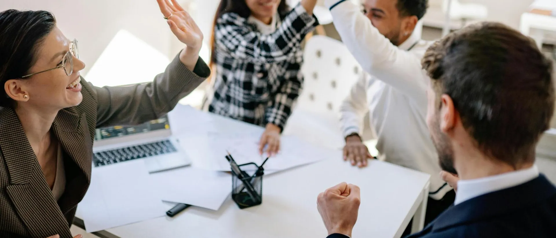 A diverse group of colleagues celebrating success in a bright office setting with high fives.