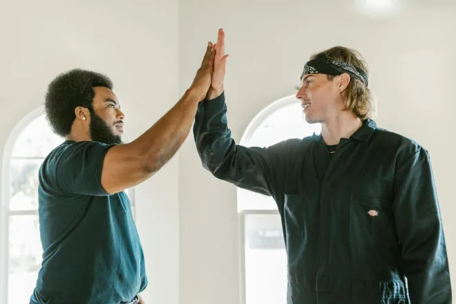 Two diverse colleagues high-five indoors, symbolizing teamwork and success.
