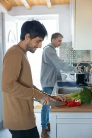 Two men enjoying cooking together in a bright, cozy kitchen, preparing fresh ingredients.