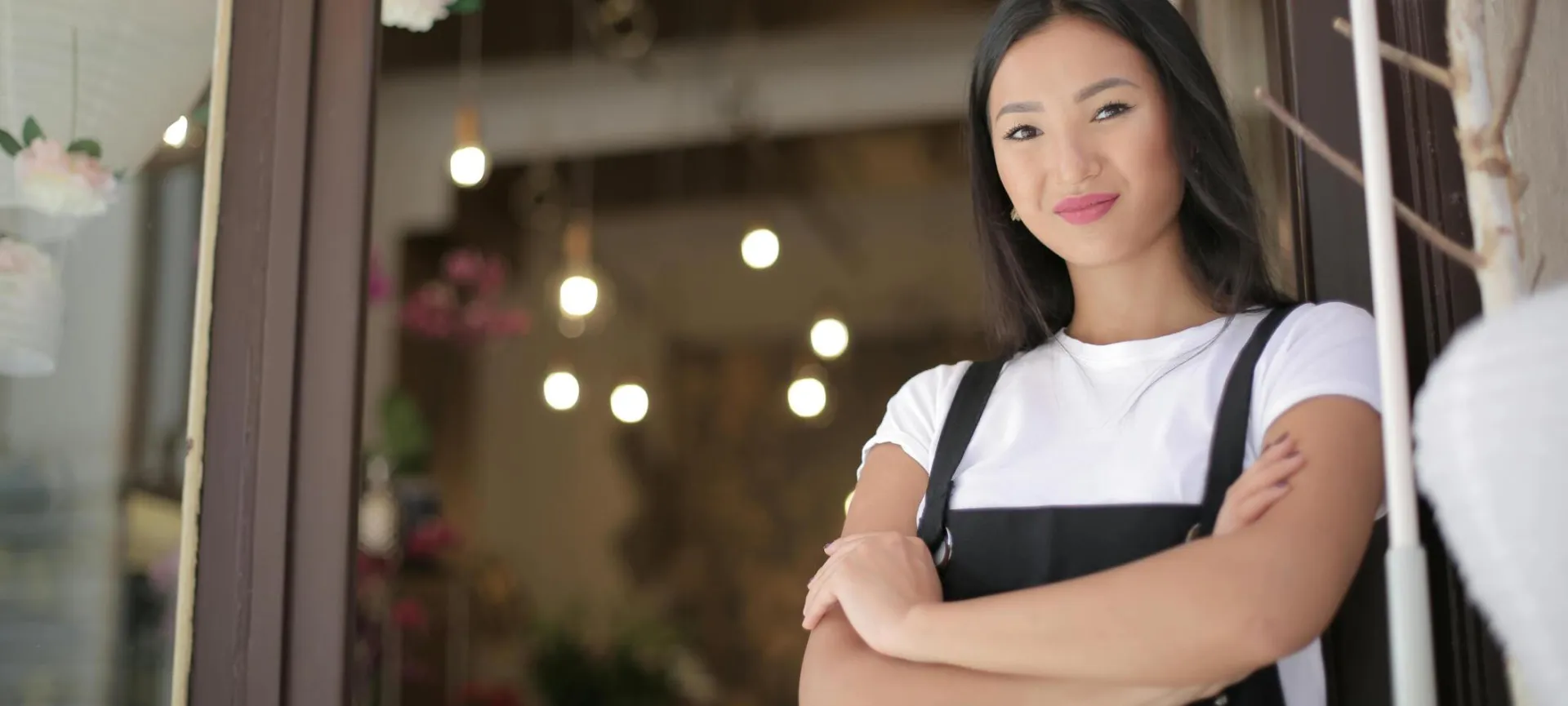 Smiling female florist standing with arms crossed at shop entrance, exuding confidence and friendliness.