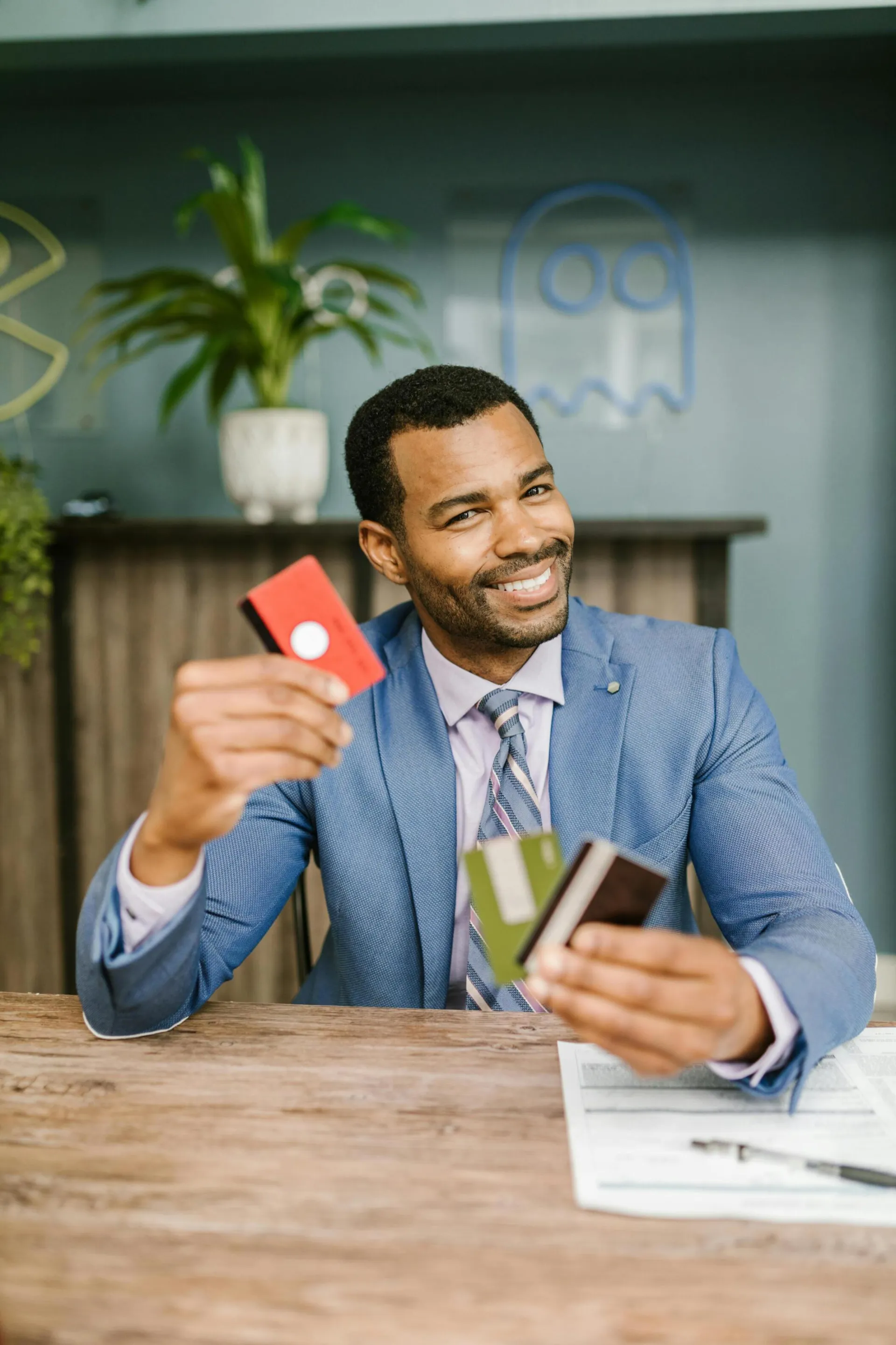 Smiling man in suit holding credit cards at a desk indoors, showcasing financial confidence.