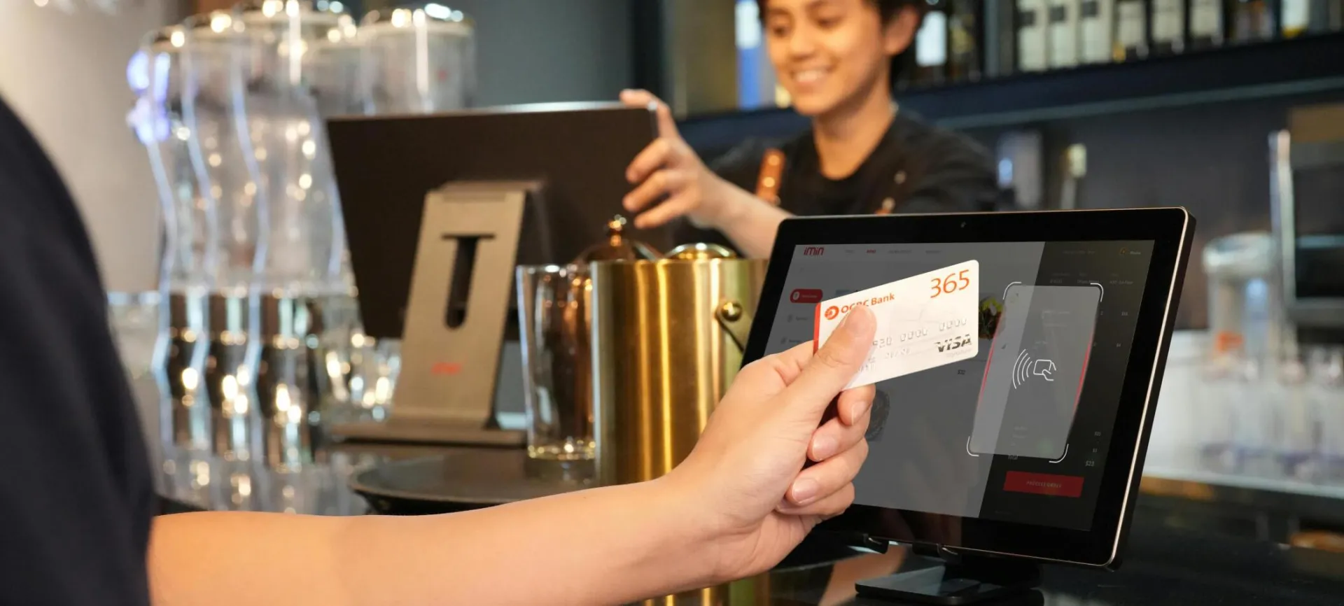 Person using contactless credit card payment at a modern bar, assisted by a cashier.