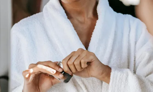 Young woman applying skincare cream in a bathrobe, reflecting self-care and wellness at home.