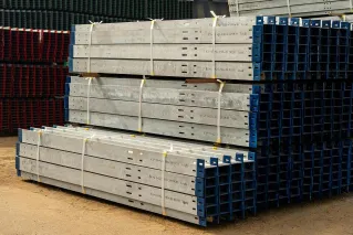 Neatly stacked metal beams in an outdoor industrial yard under daylight.