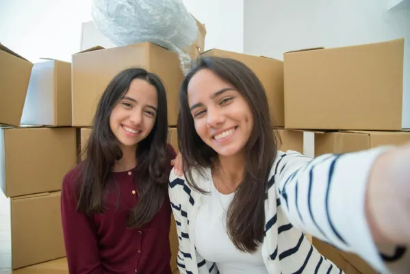 Two young women taking a selfie while moving, surrounded by cardboard boxes.